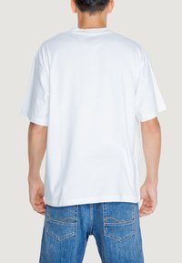 Camiseta blanca de algodón con cuello redondo, mangas cortas y un corte holgado, combinada con jeans de mezclilla azules que presentan costuras curvadas en los bolsillos.
