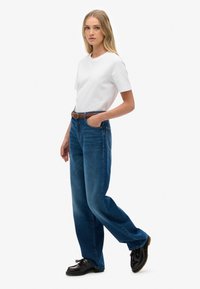 Witte katoenen t-shirt, blauw denim jeans met hoge taille, rechte pijpen, gevlochten riem, zwarte schoenen met een gestructureerd oppervlak.
