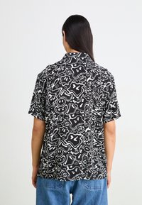 Camicia a maniche corte bianca e nera con un motivo di forme e linee astratte, dotata di colletto classico e vestibilità rilassata.