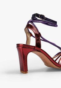 Rød metallisk højhælet sandal med lilla stropper, åben design og struktureret overflade. Udstyret med en blokhælfod og justerbar ankelsnor.