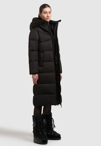 Sort puffjakke med hætte, der har en quiltet design, frontlynlås og sidelommer. Parret med sorte isolerede støvler.