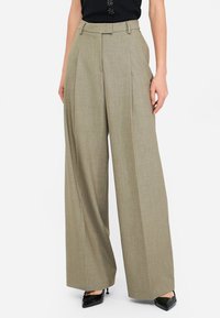 Pantaloni a gamba larga beige chiaro con pieghe, realizzati in tessuto testurizzato, caratterizzati da una vestibilità sartoriale e passanti per cintura. Indossati con tacchi alti neri.