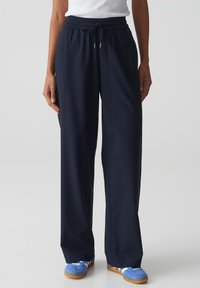 Pantalons bleu marine à taille élastique et jambes larges, avec cordon de serrage. Fabriqués en tissu doux, présentant une texture lisse et un minimum de détails.