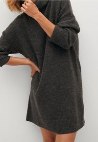 Robe en tricot surdimensionnée de couleur gris foncé avec un col haut à côtes et un tissu texturé. Présente des coutures d'épaule tombantes et des manches longues.