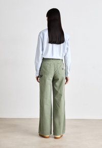 Svetle modrá košile na knoflíky v kombinaci s volnými olivově zelenými kalhotami. Kalhoty mají dvě zadní kapsy a decentní logo.