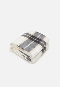 Fleece pledd, foldet. Har et mønster med grått og hvitt, akkompagnert av beige linjer. Myk tekstur, rektangulær form.