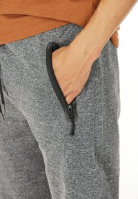 Grå texturerade joggare med en svart dragkedjeficka. Har en elastisk midja och snörning. Mjuk tyg, avslappnad design för komfort.