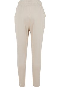 Beige Jogginghosen mit einem elastischen Bund, zwei seitlichen Taschen, zulaufenden Beinen und einer glatten, leichten Stofftextur.