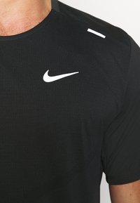 Camiseta deportiva negra de manga corta, con un logo blanco de Nike en el pecho y un pequeño acento blanco en el hombro. Textura suave.