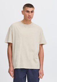 Oversized beige cotton t-shirt with a round neckline and short sleeves, featuring a small, light print on the left chest.