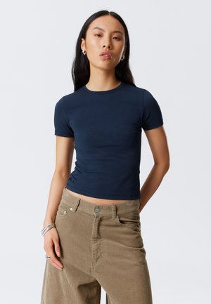Navy blue fitted t-shirt with short sleeves and a crew neck, paired with high-waisted tan corduroy pants. Smooth texture and simple design.