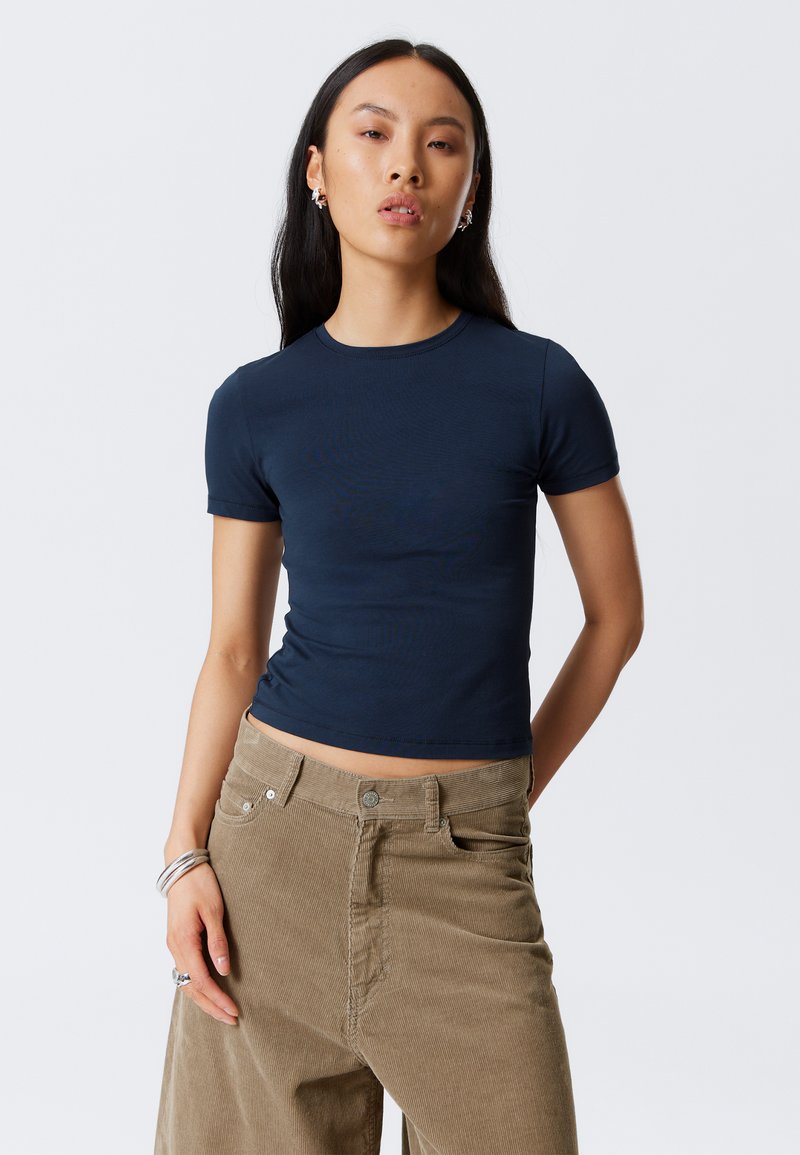 T-shirt ajusté bleu marine à manches courtes et col ras du cou, associé à un pantalon en velours côtelé beige taille haute. Texture lisse et design simple.