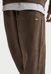 Pantalon de jogging marron en tissu doux, avec un logo Nike blanc. Le design comprend des coutures latérales et une coupe décontractée pour plus de confort.