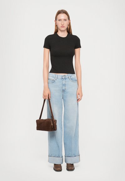 Maglietta nera aderente, jeans a gamba larga blu chiaro con risvolti, borsa in suede marrone e stivaletti con tacco marroni. Outfit semplice e casual.
