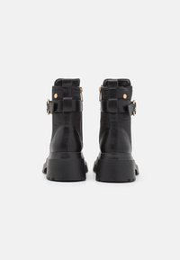 Botines negros hasta el tobillo con un exterior sintético texturizado, suela gruesa y correas decorativas con detalles en dorado.