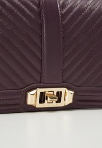 Borsa a tracolla in pelle viola scuro con trapuntatura a zigzag, accessori in oro e una chiusura rettangolare con dettaglio del marchio sulla parte inferiore.