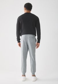 Zwarte lange mouwen shirt, grijze trainingsbroek met elastische boorden en witte sneakers. Soepele stof en een relaxed fit met details op de achterzak.