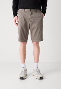 Khaki šortky z bavlněné směsi, ke kolenům, s viditelným zapínáním na knoflík, bočními kapsami a hladkým povrchem. Oblečeno s šedými teniskami.