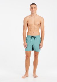 Turquoise zwembroek met zwarte zijaccenten, elastische tailleband en trekkoord. Lichtgewicht stof, ontworpen voor comfort en mobiliteit.