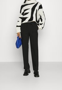 Musta räätälöity housut yhdistettynä lyhytlahkeiseen valkoiseen neuleeseen, jossa on rohkeat mustat ja kermaiset raidat. Sininen laukku viimeistelee ilmeen.