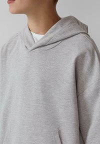 Grijze katoenen hoodie met een trekkoord in de capuchon, zachte textuur en een buidelzak. Heeft een relaxte pasvorm en minimale stikdetails.
