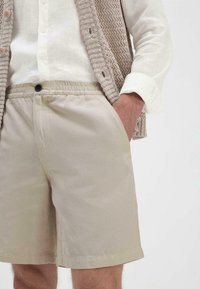 Beige katoen shorts met een elastische tailleband en zijzakken, gecombineerd met een lichtbeige gestructureerde gebreide vest.