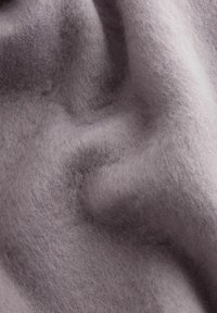 Pehmeast villast kangast heledas hallis, millel on tekstuur ja luksuslik välimus, kus on voldid ja pehmed kontuurid, rõhutades selle paksust ja soojust.