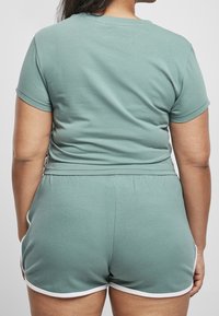 T-shirt di cotone verde con maniche corte, abbinata a pantaloni corti verdi con bordi bianchi. Tessuto morbido e vestibilità rilassata.