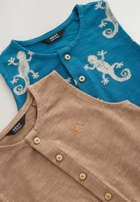 Dos chalecos: uno turquesa con estampado de lagarto blanco, botones y cuello redondo; otro beige con bordado de sol y botones, tejido texturizado.