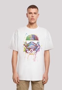 Fehér pamut póló, amelyen egy színes grafika látható, Stormtrooper sisak mintával, körülötte kék, zöld, sárga és rózsaszín fröccsenésekkel.
