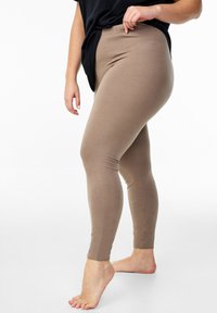 Leggings beige realizzati in un morbido tessuto elasticizzato, con una vita alta e una texture liscia, indossati con una maglia nera ampia.