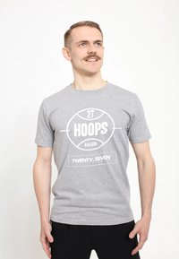 Šedé bavlněné tričko s krátkými rukávy; na přední straně se nachází bíle vytištěný text "27 HOOPS BALLERS" a "TWENTY-SEVEN" v obdélníkovém rámečku.