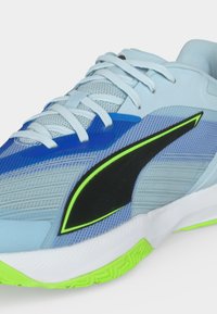 Hellblauer Sportschuh mit weißen Schnürsenkeln, dunkelblauen und neongrünen Akzenten sowie einer strukturierten Sohle mit neongrünem Profil.
