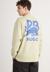Hosszú ujjú, világoszöld ing, laza szabással. A hátsó részen egy nagy, kék bika grafika és a "PB HUGO" felirat található. Puha szövet tapintás.
