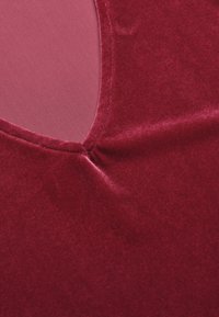 Burgundy samettikangas, jossa on sileä rakenne ja syvälle uurrettu kaula-aukko. Ominaisuuksina on rypytetty sauman yksityiskohta kaula-aukon reunassa.