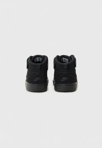 Svarte mid-top sneakers med teksturert stoff, polstret krage, borrelåsrem og gummisåle; logo på hæl og side.