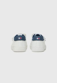 Hvite sneakers med en glatt lærfinish, marineblå hælaccents og logopatch. Har flate lisser og en gummisåle.