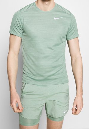 Man die een lichtgroen Nike sportshirt met korte mouwen en bijpassende korte broek draagt, met zichtbare Nike-logo's op de borst en linkervoet.