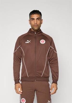 Brun atletisk jakke med høj krave, hvide accenter og logo-patches, med lynlås og ribbede manchetter.