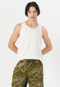 Top din bumbac alb, cu nervuri, cu un decolteu larg, asortat cu șorturi verzi măslinii, decorate cu broderie florală albă și o talie elastică.