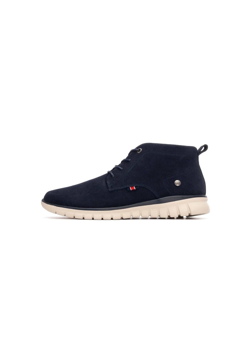 Botas de ante azul marino hasta el tobillo con suela de goma beige, con punta redonda, cordones y un pequeño acento de logotipo en el lateral.