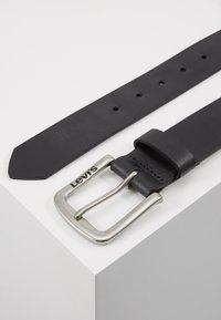 Cinturón de cuero negro con una hebilla de metal plateado. Presenta múltiples agujeros para ajuste de tamaño y el logotipo "Levi's" en relieve cerca de la hebilla.
