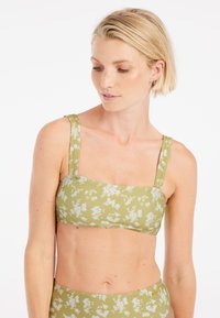 Zelený bikiny top s kvetinovým vzorom, s ribbed textúrou, štvrtkovým výstrihom a širokými ramienkami. Dizajn obsahuje biele kvetinové akcenty.