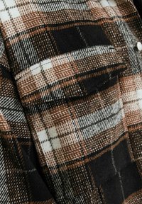 Brown and black plaid flannel shirt with a textured wool-like fabric; features a chest pocket and white buttons.