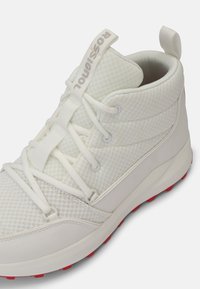 Sneakers bianchi alto con una parte superiore in rete testurizzata, lacci elastici e suola in gomma rossa. Presentano un'etichetta con il logo sul colletto.