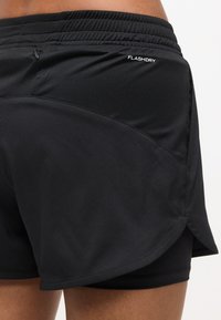 Κοντινό πλάνο μαύρων αθλητικών σορτσών με ενσωματωμένη στρώση συμπίεσης και ελαστική μέση με την επισήμανση "FLASHDRY."