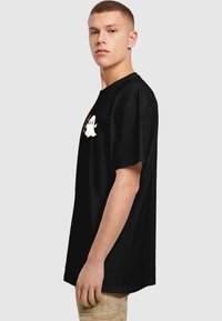 Black cotton t-shirt with a loose fit, featuring a white ghost graphic with orange accents on the chest, visible seams, and short sleeves.