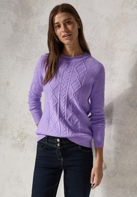 Pull en maille lavande avec un motif en diamant texturé et un col rond, associé à un jean foncé avec deux boutons et des surpiqûres contrastées.