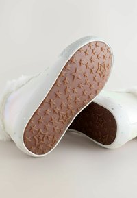 Bottes d'hiver blanches avec un col en fausse fourrure, des accents pailletés et des semelles en caoutchouc à motif étoilé, présentées sur un fond neutre.