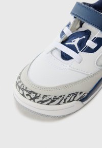 Weiße und graue Sneaker mit einem strukturierten grauen Akzent und einem blauen Riemen. Ausgestattet mit weißen Schnürsenkeln, einem blauen Zungenpatch und einem gestreiften Muster ähnlich einem Zebra.